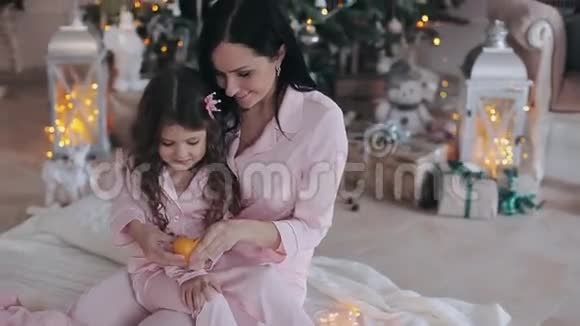 妈妈和漂亮的小女孩在圣诞树附近吃橘子视频的预览图