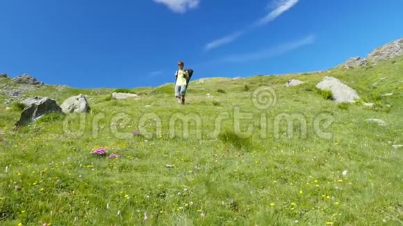 女人在田园诗般的山景中跋涉在小径上穿越盛开的绿色草地在高高的岩石山中响起视频的预览图
