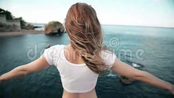 这位年轻女子举起她的手迎着太阳迎着大海岩石和天空伴着云彩视频的预览图