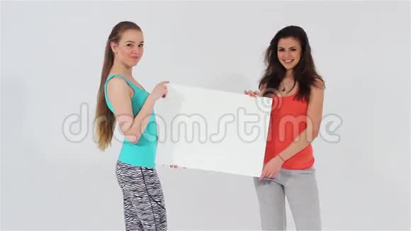 两个微笑着迷人的女孩和衬衫拿着白色的空白横幅视频的预览图