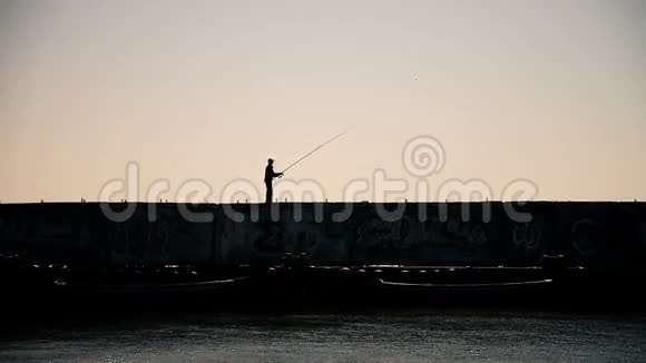 日落时分一名男子从有工业背景的防波堤上钓鱼视频的预览图