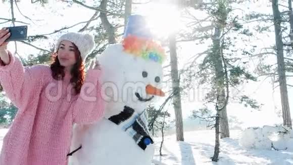 可爱的女孩和雪人合影冬天的自拍手机在手的一个年轻女人做有趣的自拍照片在里面视频的预览图