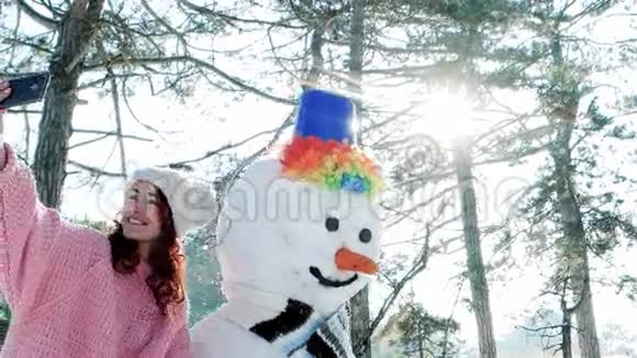 冬天自拍可爱的女孩和雪人合影一部手机在年轻女人的手中玩自拍照片在里面视频的预览图