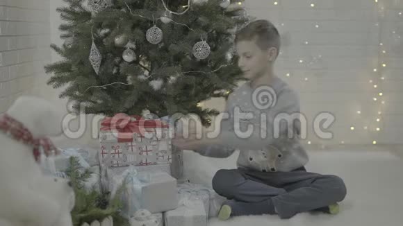 欢乐的小男孩在装饰的新年树节日气氛室内打开圣诞礼物盒视频的预览图