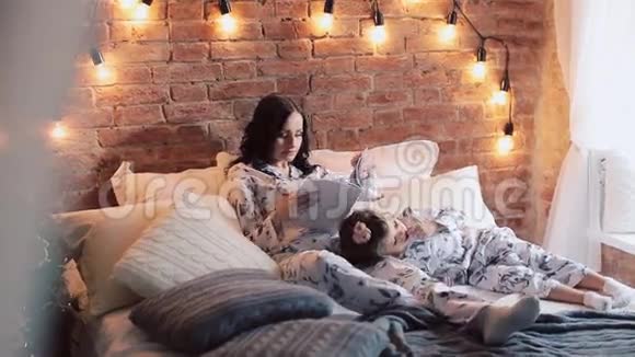 家庭阅读睡觉时间漂亮的年轻母亲在给女儿读一本书视频的预览图