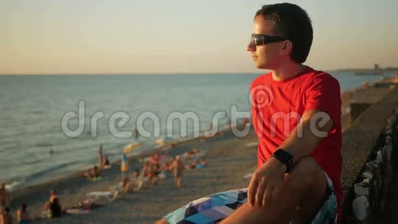 年轻的帅哥戴着太阳镜在日落时在海边放松他欣赏日落和水在转弯之后视频的预览图