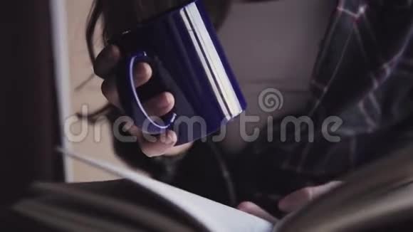 特写镜头中年轻女性手拿着一本打开的书和一杯热饮料视频的预览图