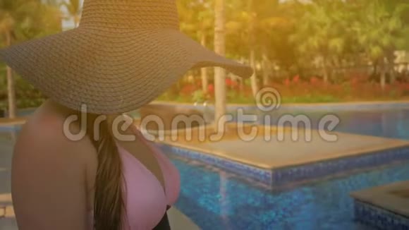 戴着蓝帽子的漂亮女孩在游泳池边散步夏日的阳光慢动作视频的预览图