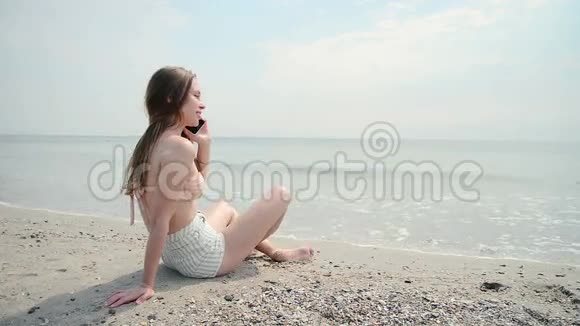 女孩坐在海滩上在手机上留言视频的预览图