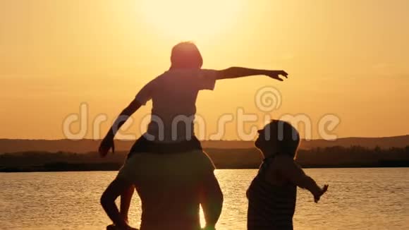 日落时湖岸幸福家庭的剪影视频的预览图