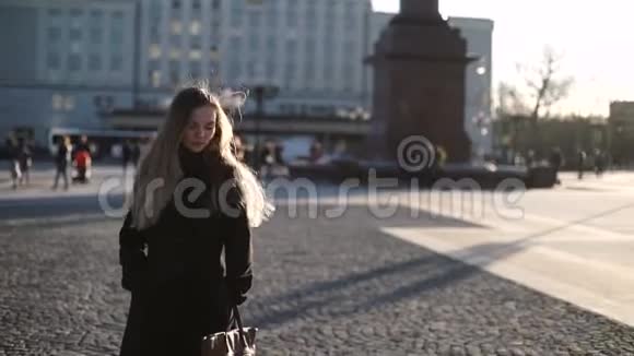 年轻的美女身穿灰色外套留着长发在日落时分在市中心的时装模特身上微笑着摆姿势视频的预览图
