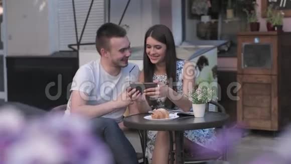 一个男人的女人在一家夏日咖啡馆里看着智能手机上的照片视频的预览图
