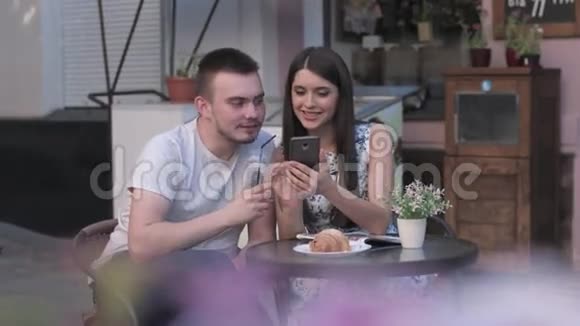 一个男人的女人在一家夏日咖啡馆里看着智能手机上的照片视频的预览图