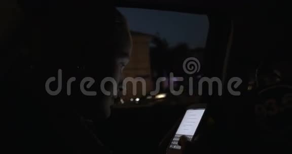 在城市里一个年轻的女人在夜间开车时用手机视频的预览图
