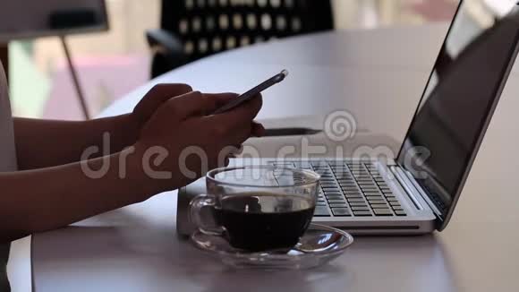 女性在办公室的笔记本电脑上使用智能手机用杯子喝茶视频的预览图