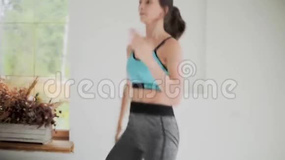 年轻健康的黑发女孩穿蓝色上衣紧身裤在明亮的房间里做运动在家做运动和健身训练视频的预览图