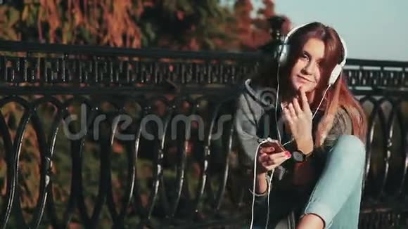 耳机美丽的女孩在城市公园的耳机里放松和听音乐戴着耳机的女人视频的预览图