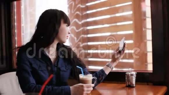 小女孩在咖啡馆的智能手机上自拍手持的视频的预览图