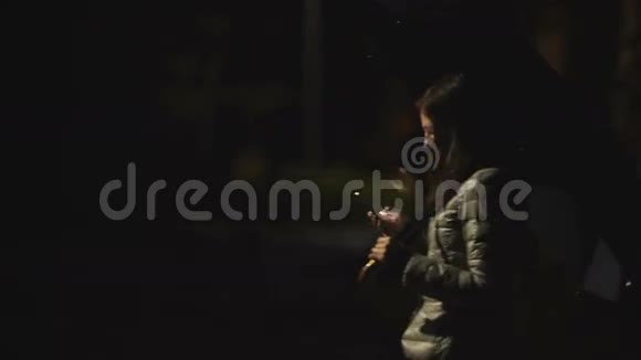 带雨伞的女孩晚上在城市背景中使用手机视频的预览图