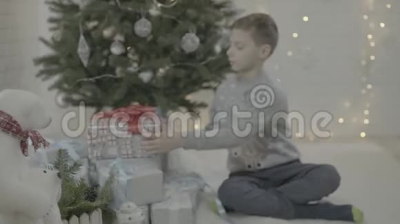 快乐的小男孩打开圣诞礼物盒装饰新年树节日气氛室视频的预览图