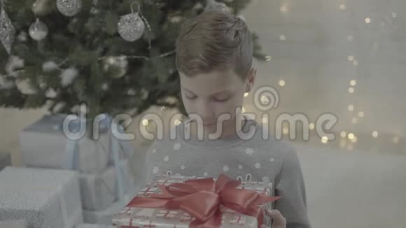 欢乐小男孩在装饰的新年树节日气氛室内打开圣诞礼物盒视频的预览图