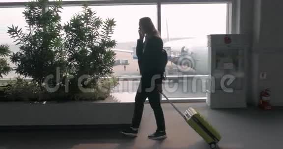 带着手提箱的女人打电话在机场候机楼散步视频的预览图