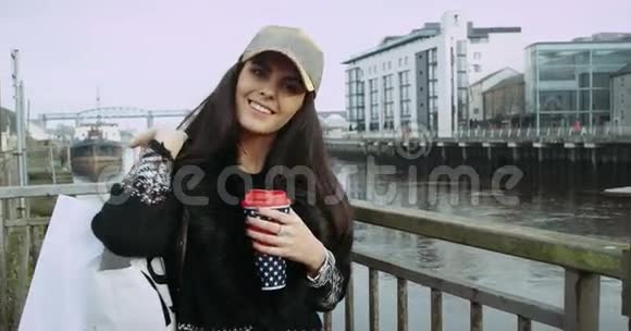 美丽微笑的黑发女士脱下她的夹克走在桥上河的背景4k视频的预览图