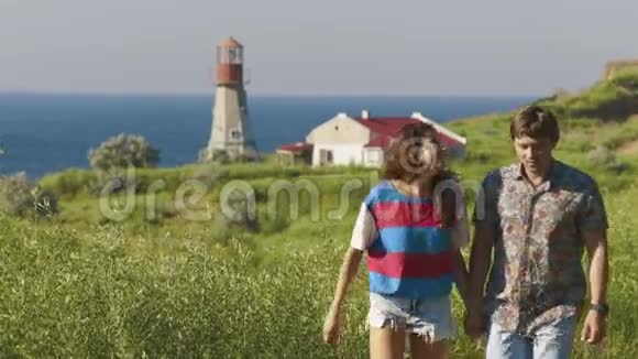 年轻的一对夫妇走到一起在海滨悬崖的灯塔附近谈笑风生慢动作视频的预览图