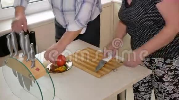 一位年长的男人和一位在厨房切菜的女人小心地切西红柿做沙拉健康食品概念视频的预览图
