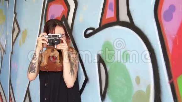 有纹身和老式相机的女孩站在涂鸦墙附近视频的预览图