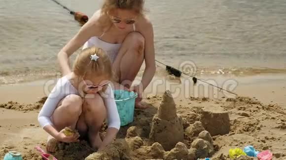 妈妈和女儿正在海滩上玩耍建造一座沙堡夏日阳光明媚假期视频的预览图