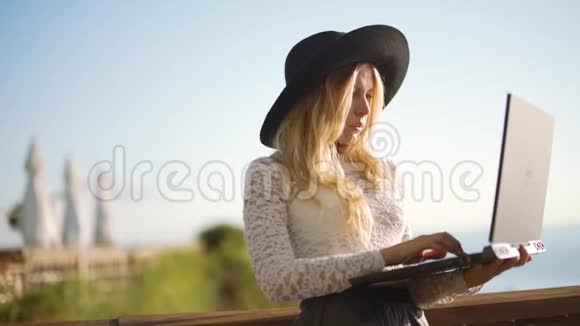 年轻的女人带着笔记本电脑坐在海边的咖啡馆里工作视频的预览图