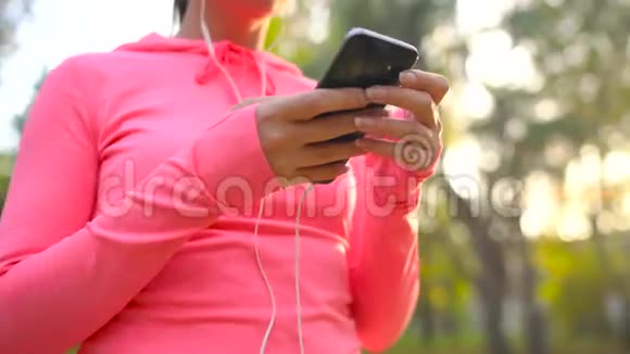 带着耳机和智能手机的女人选择音乐穿过秋天公园视频的预览图