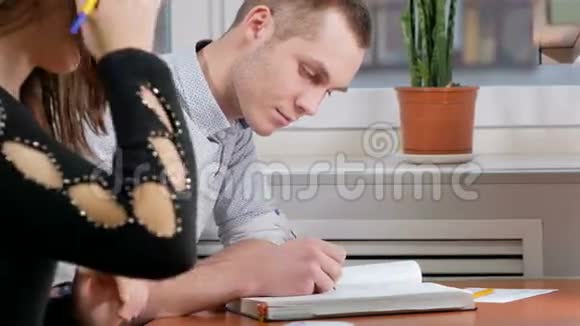男学生建议妇女如何正确地在笔记本上写下一些东西一个棕色头发的女人仔细地写着视频的预览图