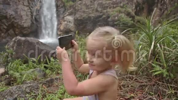 特写小女孩在石头上打电话对抗瀑布视频的预览图