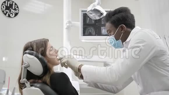 年轻的非裔美国男医生戴着医疗面具的牙医在牙科诊所的椅子上有个漂亮的女病人医药视频的预览图