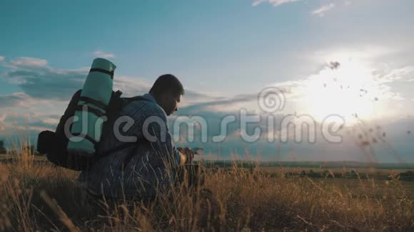 一个带背包的年轻游客使用手机在夕阳的光芒中旅行概念一直在线视频的预览图