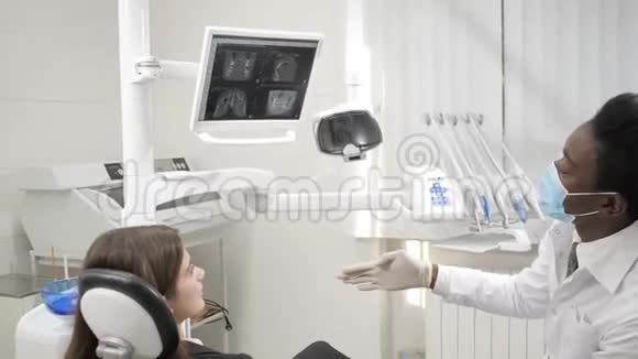 年轻的非裔美国男医生戴着医疗面具的牙医在牙科诊所的椅子上有个漂亮的女病人医药视频的预览图