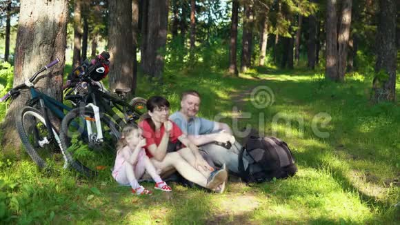 这家人在阳光明媚的日子里骑自行车在夏天的森林里休息视频的预览图