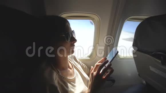 日落时分坐在飞机窗口附近的旅游妇女在飞行中使用手机视频的预览图