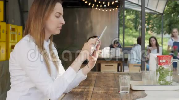 年轻漂亮的商务女性在户外咖啡厅午休时使用平板电脑视频的预览图