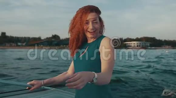 快乐的红发女孩穿着绿松石裙在摩托艇上跳舞去摇头发笑笑视频的预览图