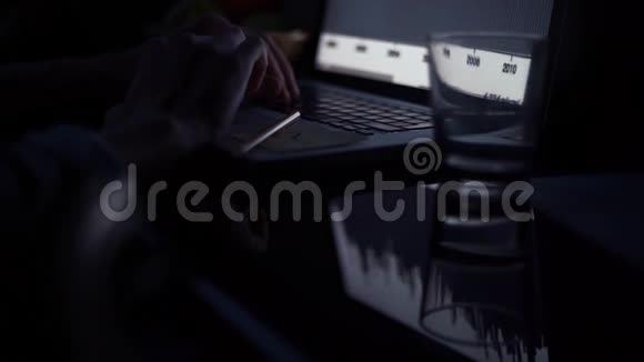 晚上在厨房用笔记本电脑的年轻人桌子上有一杯水和铅笔视频的预览图
