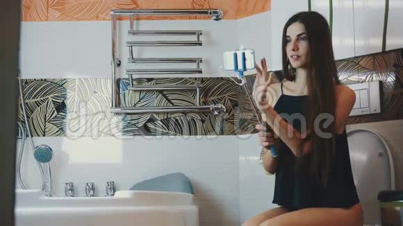 布鲁内特女孩坐在厕所在浴室持有智能手机蓝色莫诺波德视频的预览图
