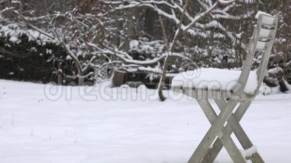 花园里覆盖着雪的塑料椅子和背景上的雪花飘落视频的预览图