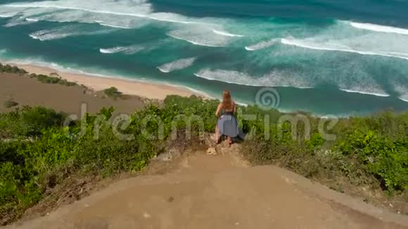 一名年轻女子在巴厘岛的一个偏僻的海滩上游览的空中镜头站在岩石上看着一个视频的预览图