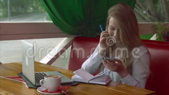 一位在咖啡馆工作的商务女性她用智能手机和笔记本视频的预览图