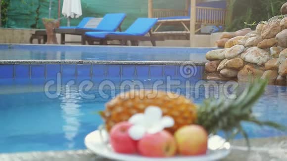 在游泳池后面的盘子里放着不同的水果菠萝苹果美丽的弗拉吉帕尼花视频的预览图
