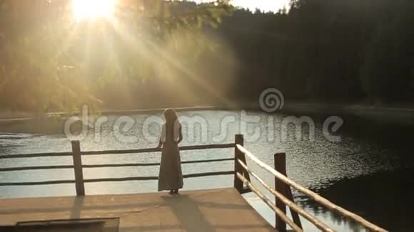 留着乌族服饰深色长发的可爱女孩的后景欣赏山湖的自然景观视频的预览图