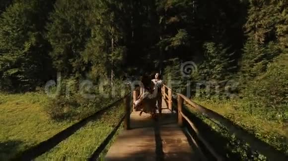 美丽而快乐的一对夫妇在木桥上跳舞喀尔巴阡山脉背景下的年轻男女恋爱视频的预览图
